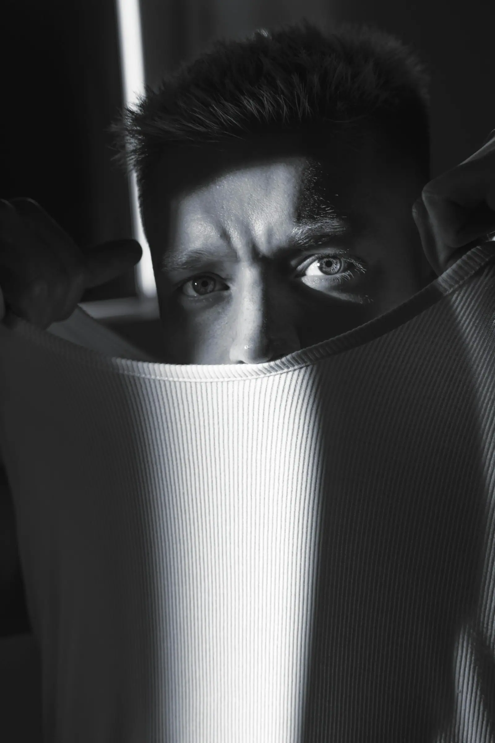 Man peeking over white shirt with dramatic lighting