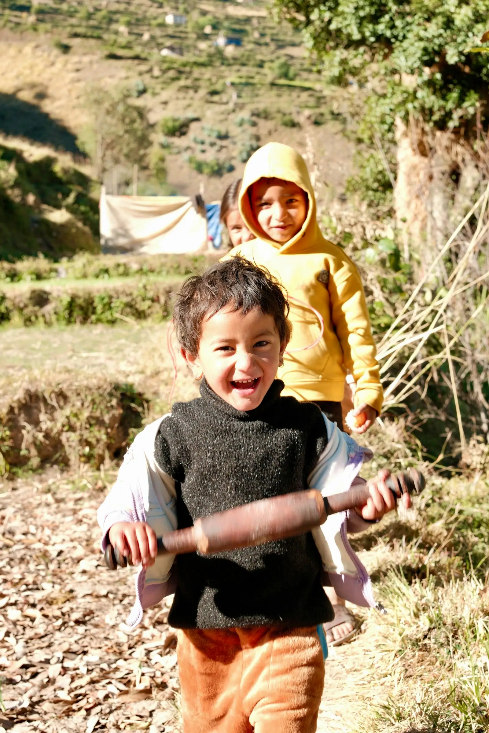 Three children walking outdoors with a rolling pin