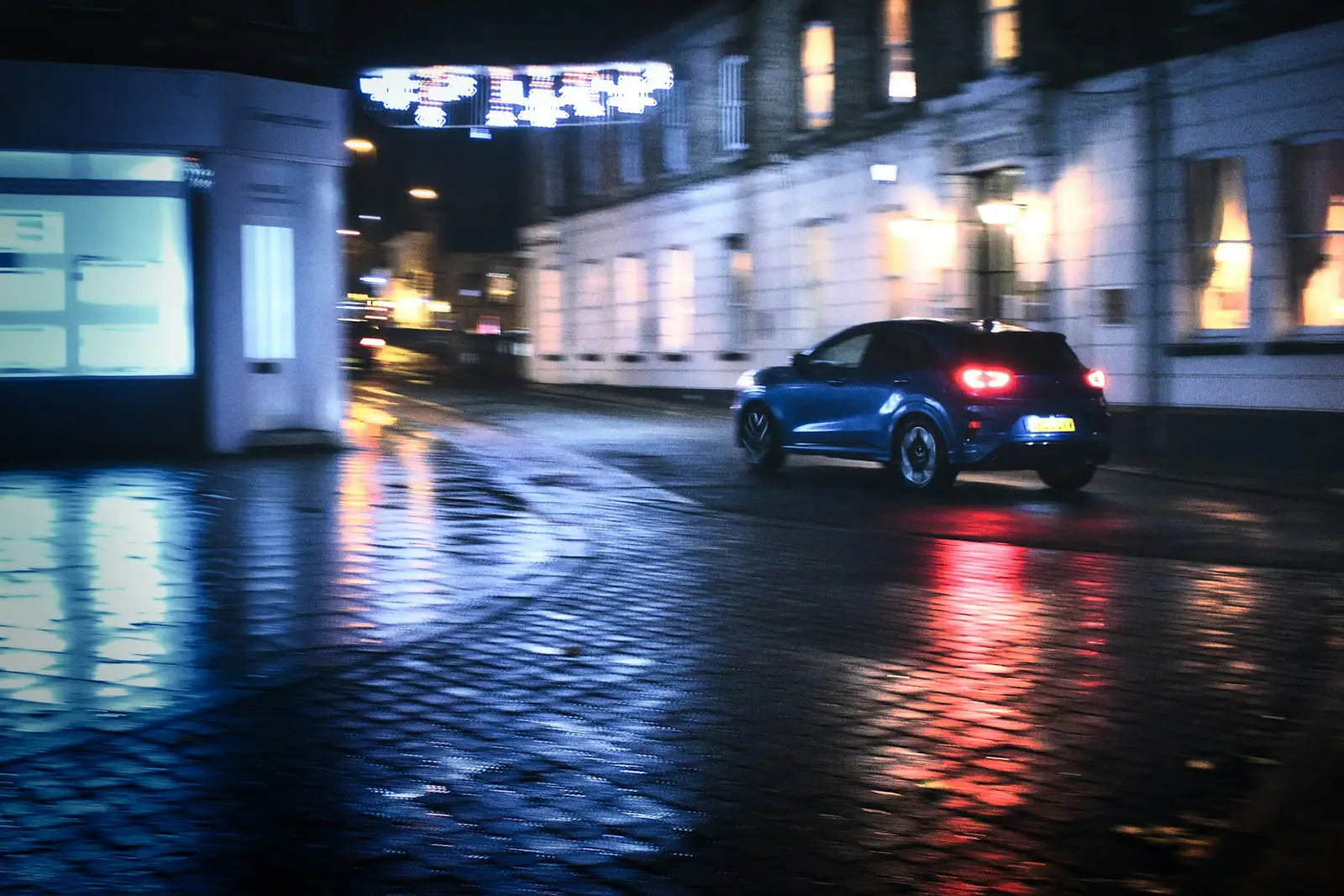A blue car driving down a street at night