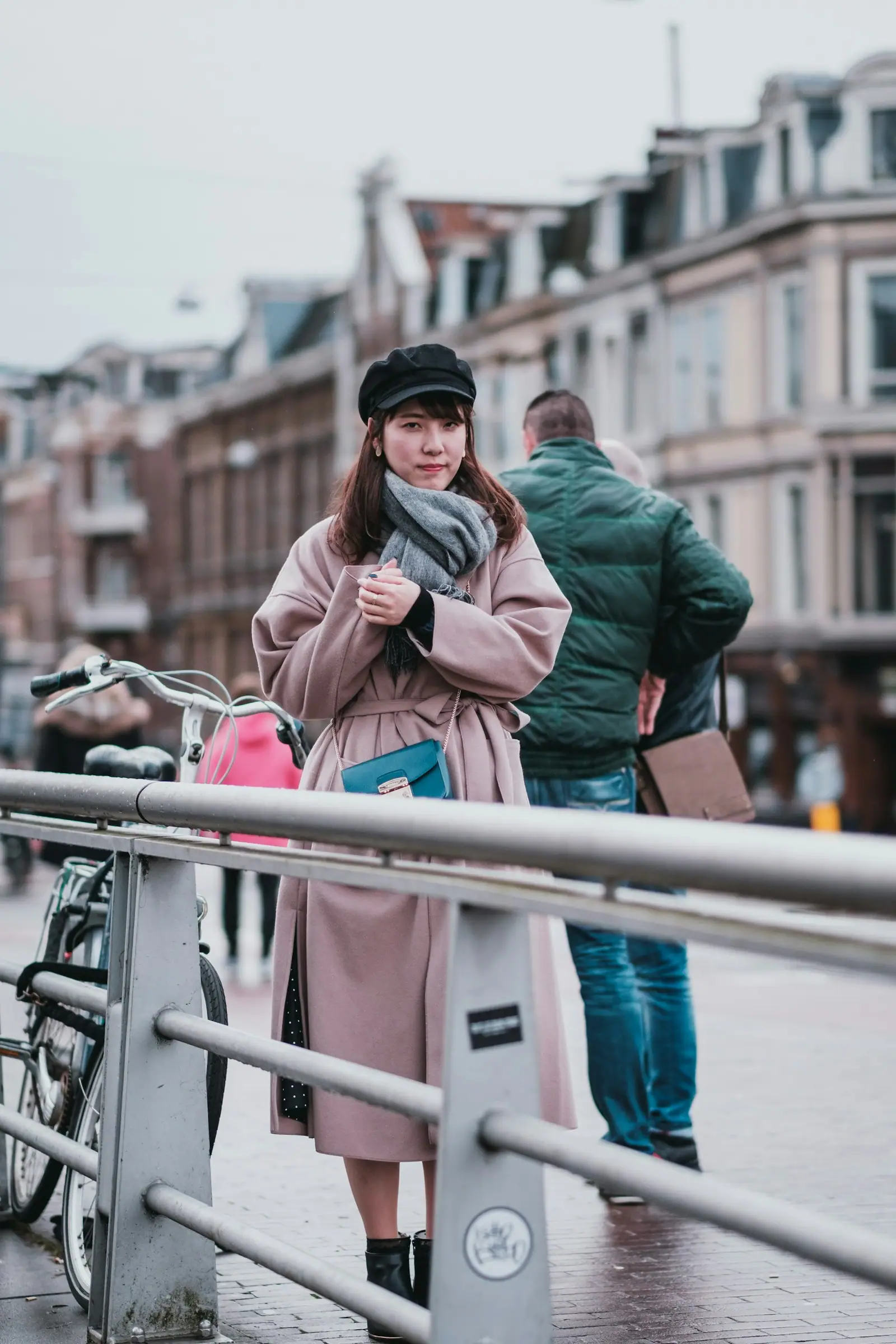 Woman in green jacket and blue denim jeans standing beside white metal railings during daytime