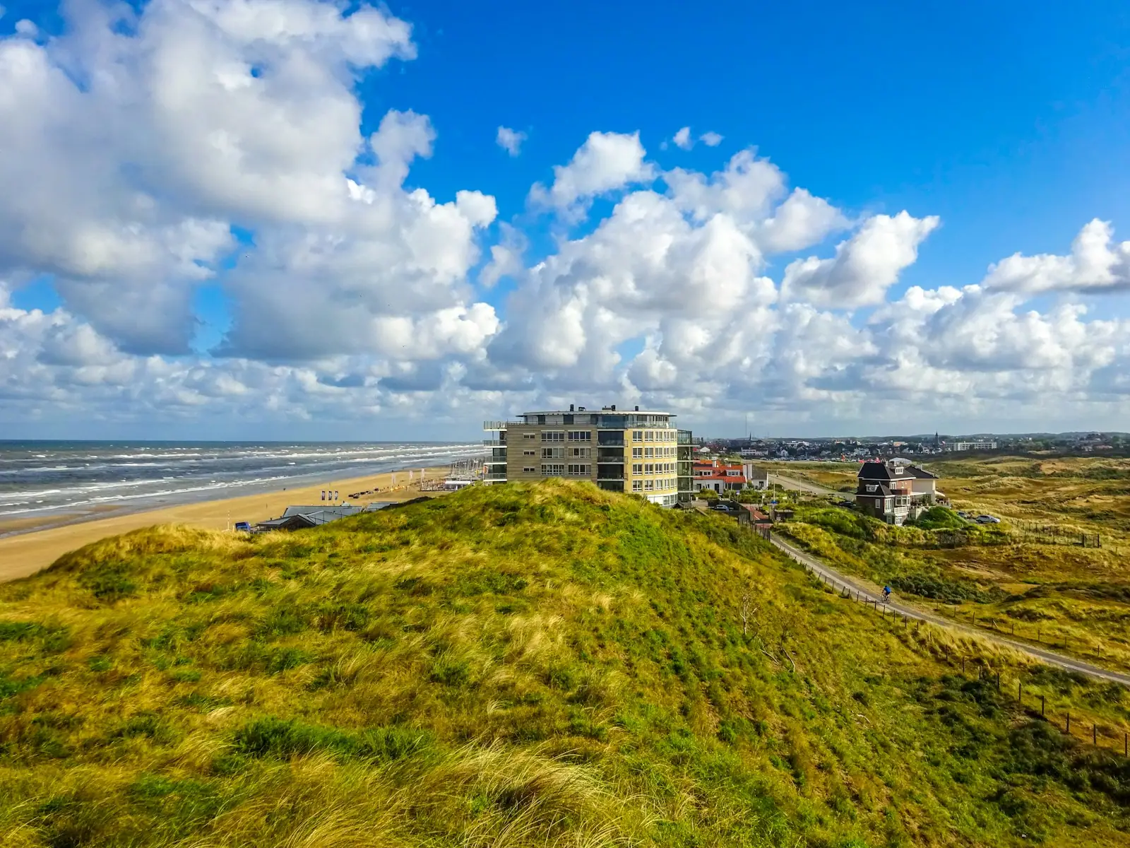 Coastal dunes with buildings and ocean under blue sky