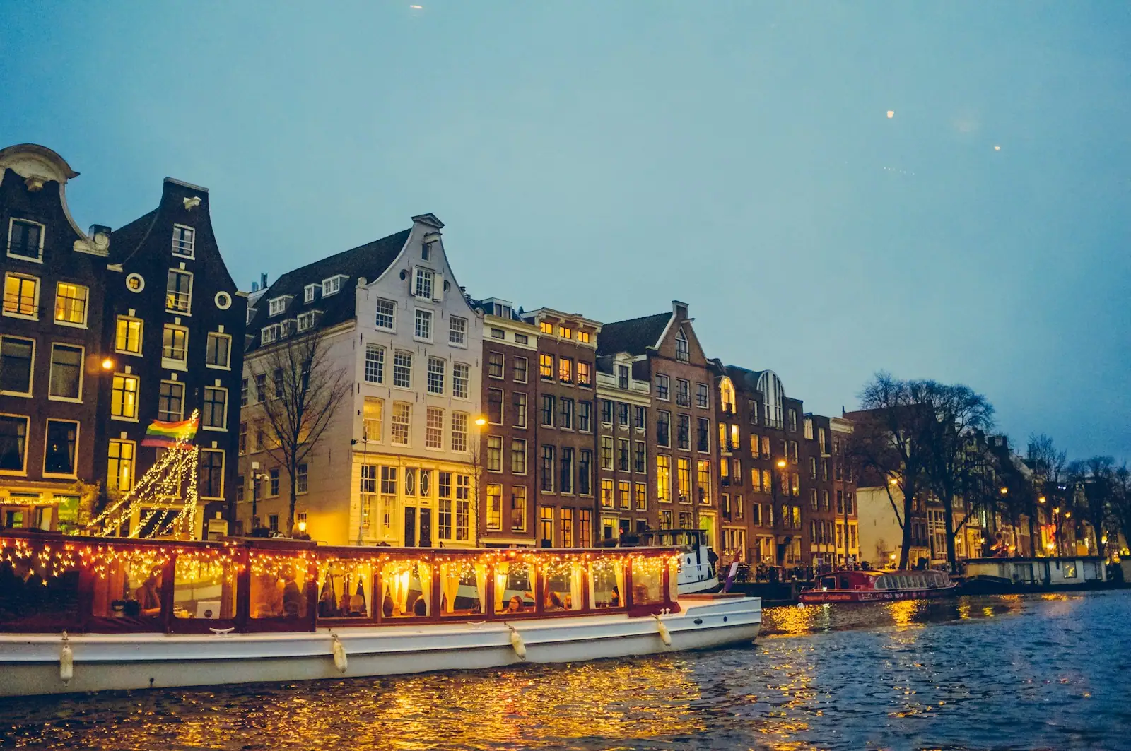 Boat sailing on river near lighted houses and trees