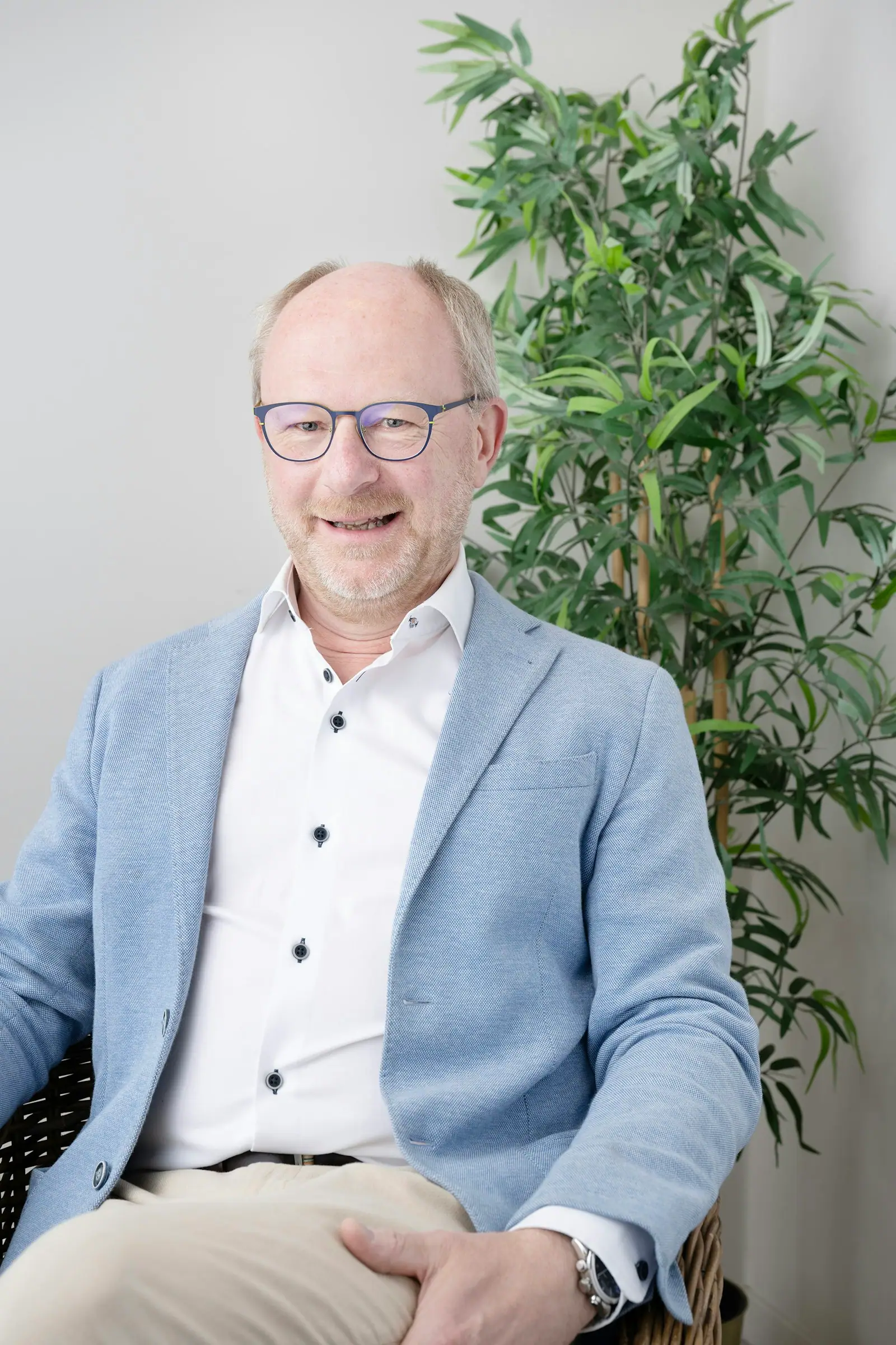 Man in blue blazer and glasses smiles indoors
