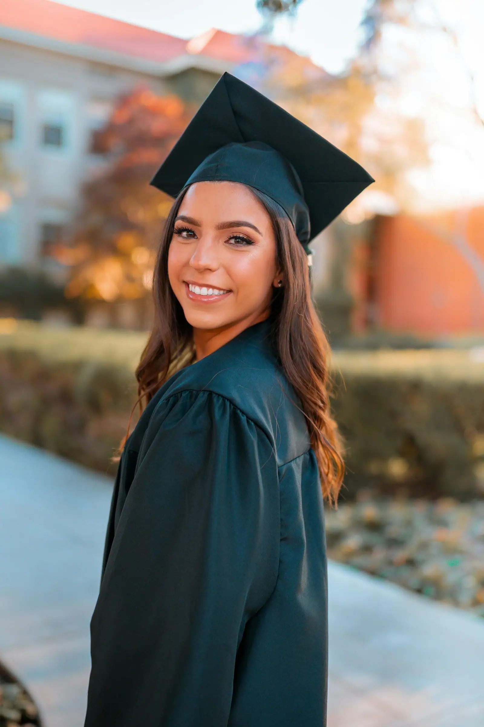 A smiling woman in a black graduation cap and gown outdoors