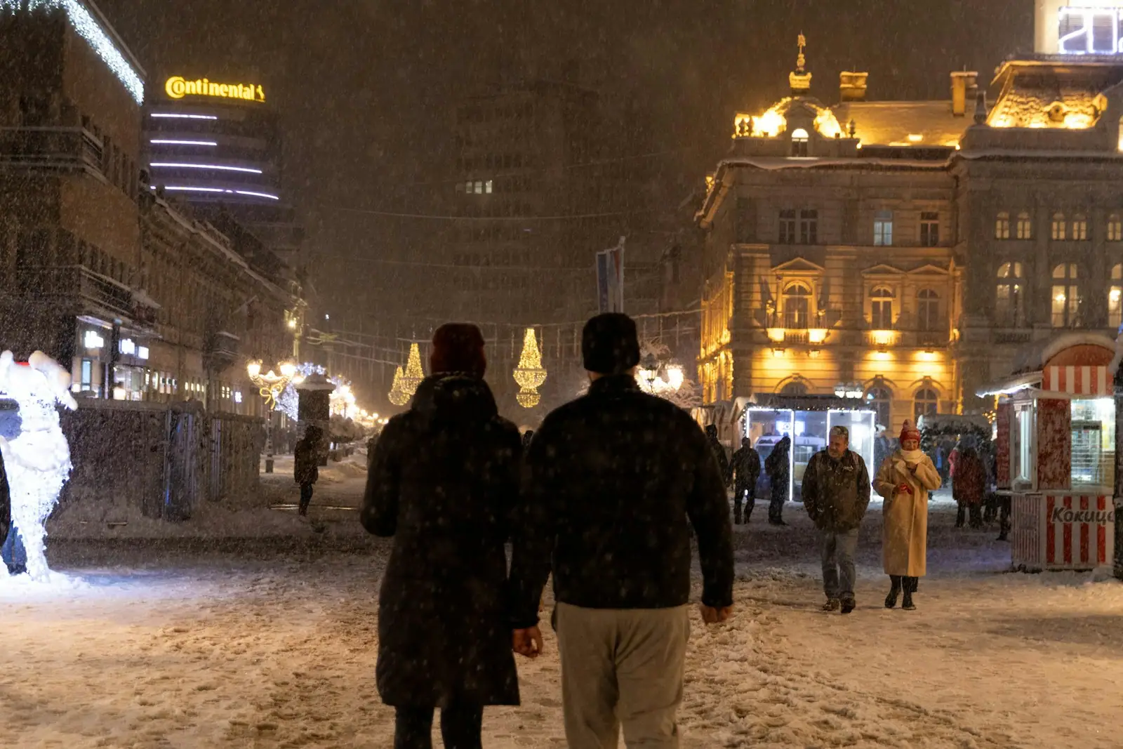 A couple walks on a snowy city street at night
