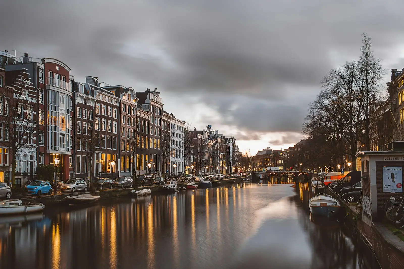 Canal lined with historic buildings and parked cars in Amsterdam at dusk