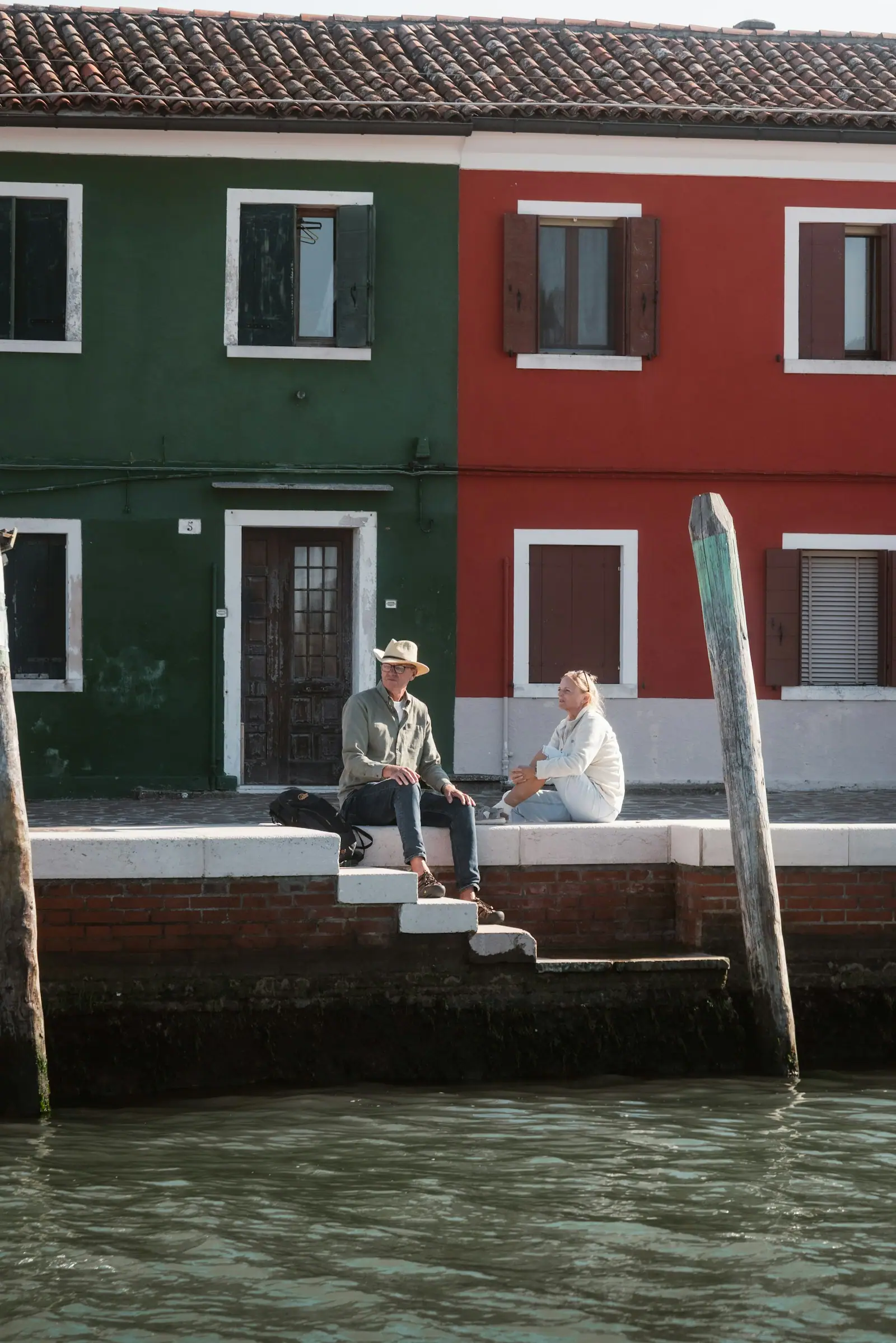 Two men sitting by a colorful building by the water